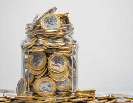 A pile of Brazilian real coins in a jar isolated on a gray backgroundの写真素材