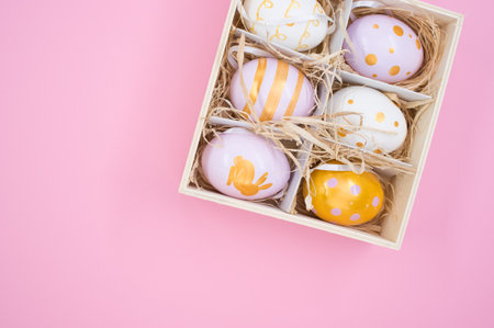 A top view of painted Easter eggs on a box with straw isolated on pink background with copy space