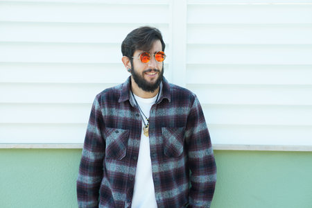 A closeup shot of a young Spanish guy wearing a checkered shirt on a wall background