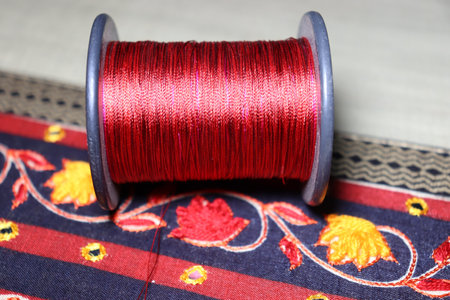 A closeup of a red yarn reel on a decorative sari cloth