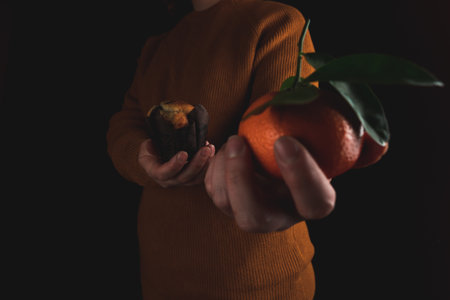A closeup view of a person holding a muffin in one and a tangerine in the other handの写真素材