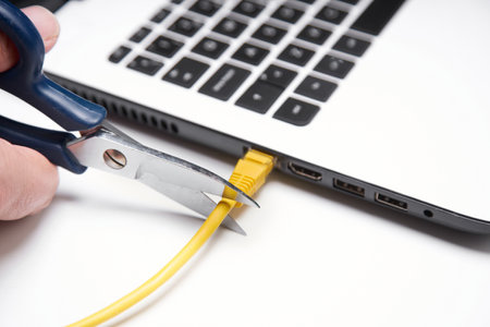 A closeup shot of a person cutting a yellow network cable with scissors connected to a laptopの写真素材