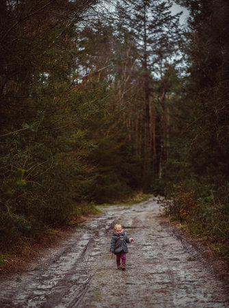 A vertical shot of a little child walking on a muddy road surrounded by treesの写真素材