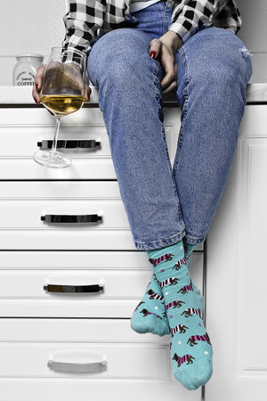 A vertical shot of a woman with a glass of wine sitting on a drawer