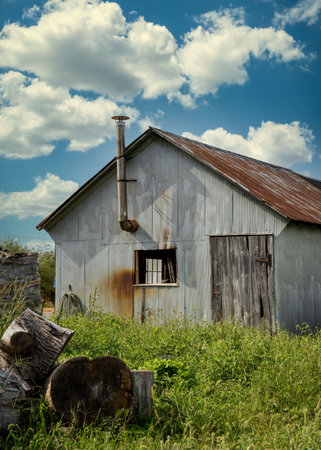 A vertical shot of an old barn in a field with a weathered roof under a cloudy skyの写真素材
