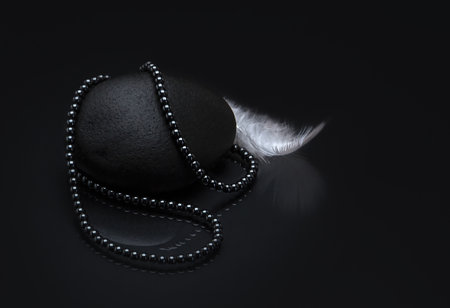 A top view of a necklace made of black pearls on black background with a white feather on the sideの写真素材