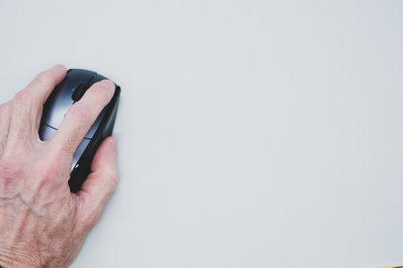 A closeup shot of an old person's and using a computer mouse on a white surface with a copy spaceの写真素材