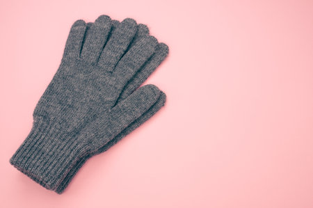 A closeup shot of black knitted winter gloves on a pink surfaceの写真素材