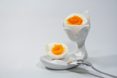 A closeup shot of a medium-boiled egg in a ceramic holder with salt and a spoonの写真素材