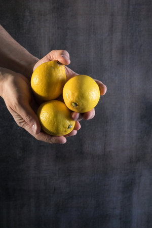 Male hands holding ripe lemon fruits in the grunge texture backgroundの写真素材