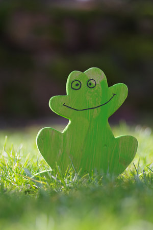 A selective focus shot of a funny green frog toy on the green grass in sunlight