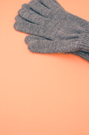 A vertical closeup shot of gray knitted pair of gloves on an orange backgroundの写真素材