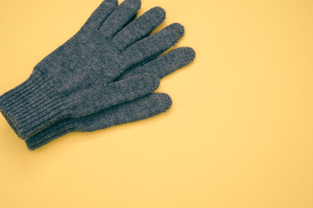 A closeup shot of gray knitted pair of gloves on a yellow backgroundの写真素材