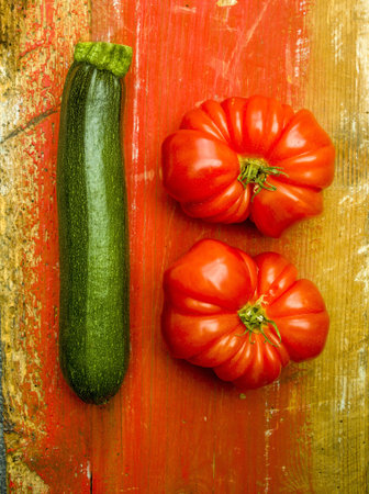 A vertical shot of a zucchini and two tomatoes on a wooden surfaceの写真素材
