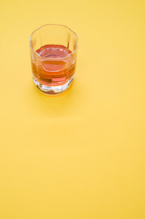 A vertical shot of a glass of whiskey on a yellow backgroundの写真素材