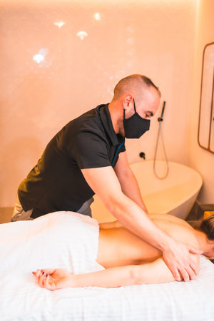 A vertical shot of a masseur performing massage therapy on a client during pandemicの写真素材
