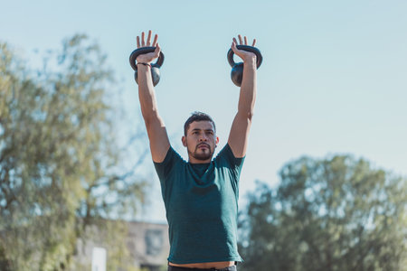 A low angle shot of a Hispanic male lifting weights outdoorの写真素材