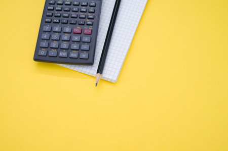 A closeup of a scientific calculator on a notebook and pencil on yellow surface for a copy space