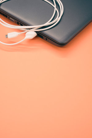 A vertical sho of a laptop with USB cable connected on a pastel orange background for a copy spaceの写真素材