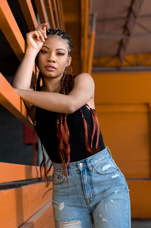 A vertical shot of a cool young Afro-American lady with deads leaning on an orange construction