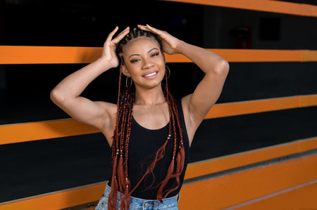 A cheerful young Afro-American lady with deadlocks standing in front of an orange and black wall