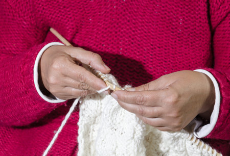 A female in a pink sweater knitting a white clothing