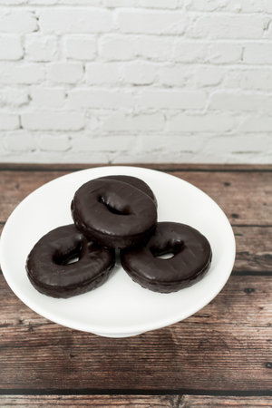 A vertical shot of delicious chocolate donuts on a white serving plateの写真素材