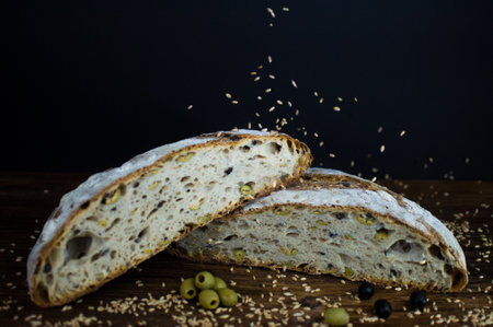 A closeup of rustic olive bread divided into two parts on black backgroundの写真素材