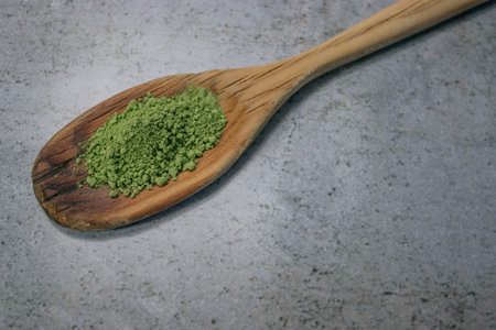 A closeup shot of green matcha tea powder on a wooden spoonの写真素材