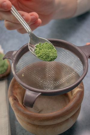 A vertical shot of a person adding green matcha tea powder in a sieve