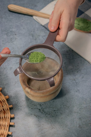 A vertical shot of a person adding green matcha tea powder in a sieveの写真素材
