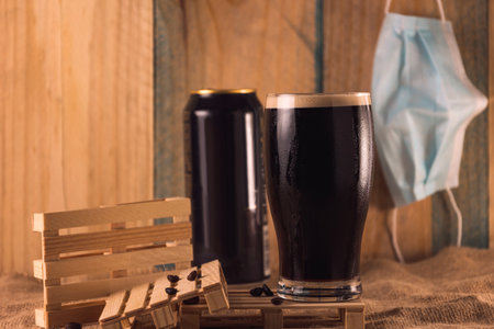 A black beer in a glass with coffee beans and a mask hanging on the wallの写真素材