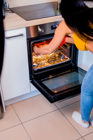 A vertical shot of a woman taking out cooked food from the ovenの写真素材