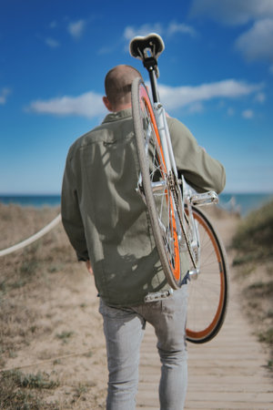 A vertical closeup shot of a male holding up his orange bike on a beachの写真素材