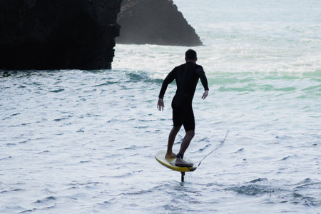 View of man riding foilboard (hydrofoil surfboard) at Piha beach, Auckland, New Zealand