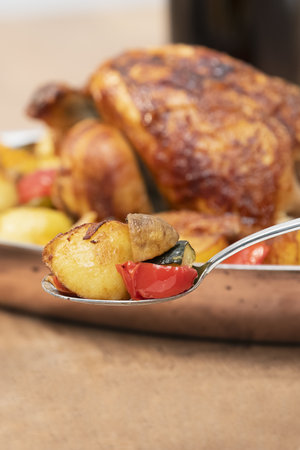 Selective focus of potato, mushroom and vegetables on a spoon with an out of focus chicken at the back. Healthy and homemade food concept.の写真素材