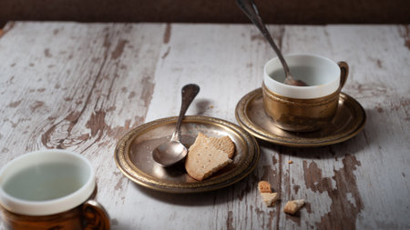 A selective focus shot of vintage coffee cups, spoons, saucers, and cookie on a weathered wooden tableの写真素材
