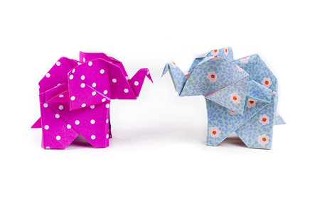 A closeup shot of two colorful patterned origami elephants standing face-to-face on a white backgroundの写真素材