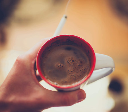 A closeup shot of a hand of a person keeping a cup of coffee with a cigaretteの写真素材