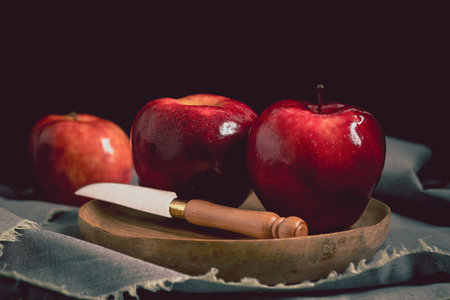 Still life with red delicious apples on a wooden plate. Three ripe apples on a wooden plate and a gray tablecloth with a wooden knife.の写真素材