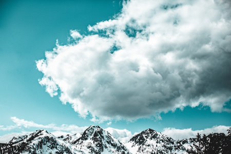 A beautiful view of high rocky mountains covered in snow under a cloudy skyの写真素材