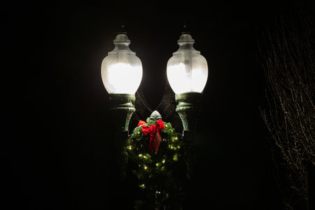 Two illuminated street lamps and a Christmas wreath on a street at nightの写真素材