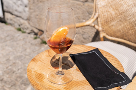 A closeup shot of a glass of cocktail with orange on a small round wooden tableの写真素材