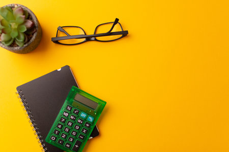 A top view of a calculator, a journal, glasses, and a plant on a yellow backgroundの写真素材