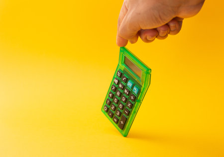 A calculator held with a finger isolated on a yellow backgroundの写真素材