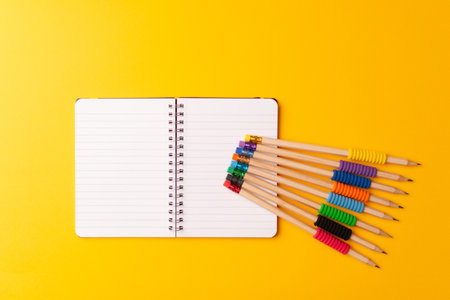 A top view of black pencils with colorful rubbers on a notepad on a yellow backgroundの写真素材