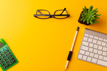 A top view of calculator, a pencil, glasses, keyboard, and a plant on a yellow backgroundの写真素材