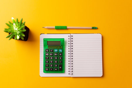 A top view of a calculator on an open journal, a pencil, and a plant on a yellow backgroundの写真素材