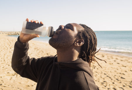 A young African-American male drinking water on a beachの写真素材