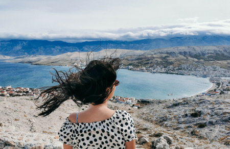 A Caucasian woman in a polka-dotted flowy dress and sunglasses with hair blown by the wind
